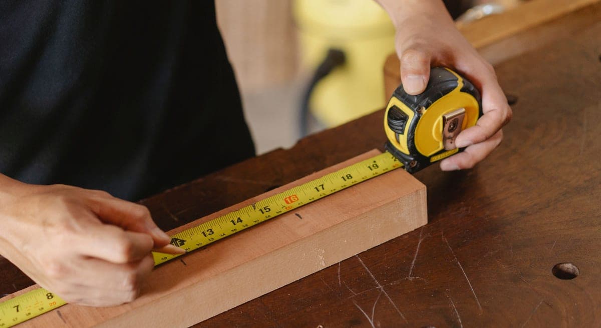 A worker marking a wooden board with a pencil and measuring tape