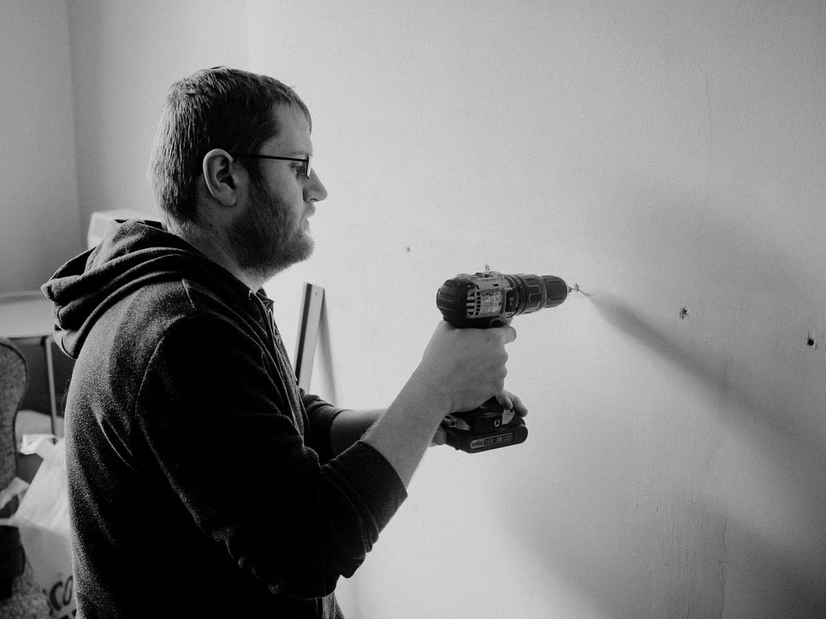 A person installing a wall-mounted shelf bracket with a drill